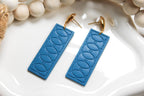 Blue textured earrings with gold hooks on a white surface with beads
