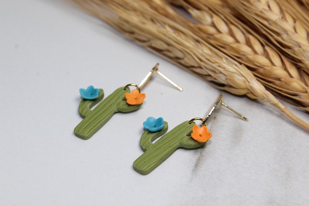 Cactus-shaped earrings with flowers on a light surface with straw background