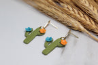 Cactus-shaped earrings with flowers on a light surface with straw background