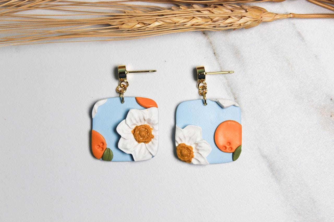 Pair of floral and peaches earrings on a light background with dried grass.
