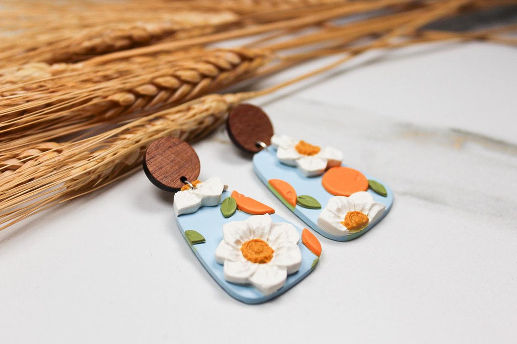 Pair of floral-themed and peach earrings with wooden and colorful components on a light surface.