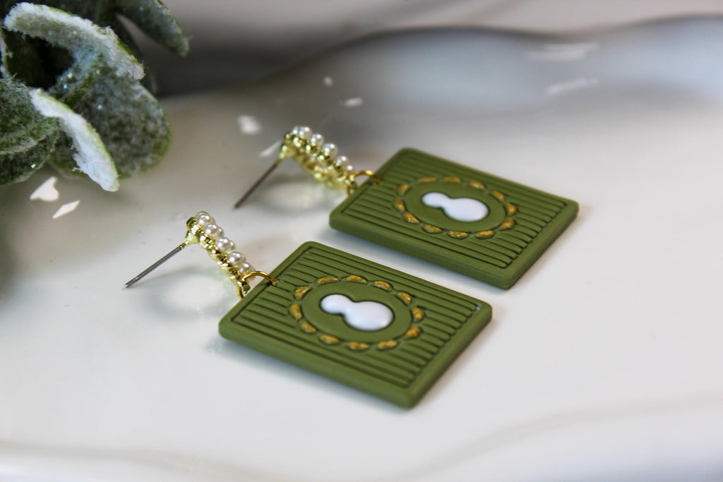 Green rectangular earrings with white snowman design on a light background