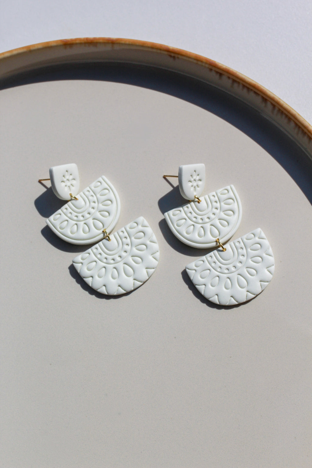 White ceramic earrings with gold accents on a light gray surface.