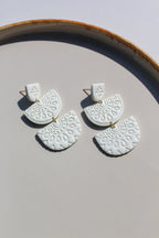 White ceramic earrings with gold accents on a light gray surface.