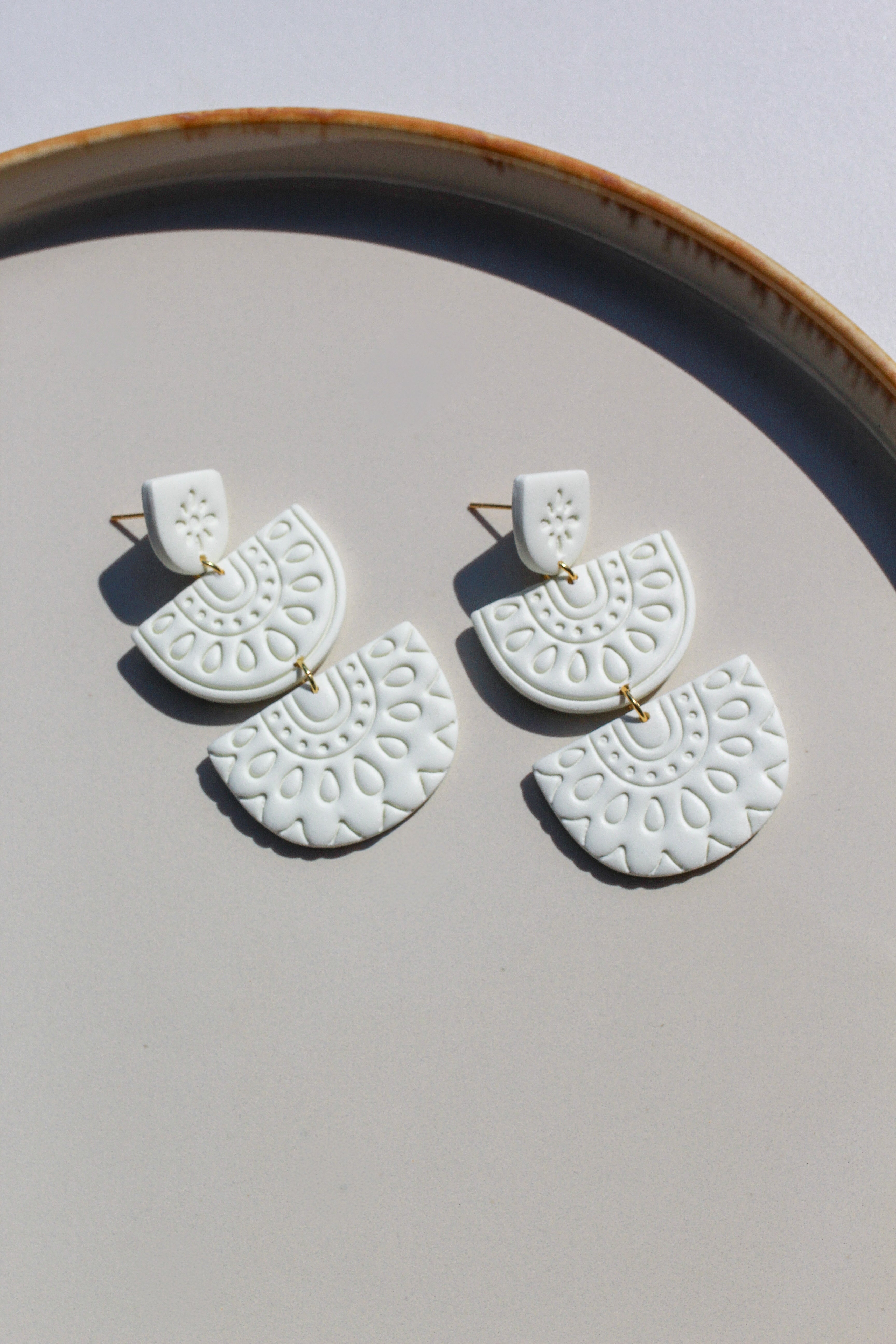 White ceramic earrings with gold accents on a light gray surface.