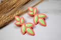 Neon green and pink leaf-shaped earrings on a light background with dried grass.