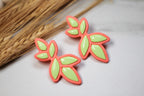 Neon green and pink leaf-shaped earrings on a light background with dried grass.