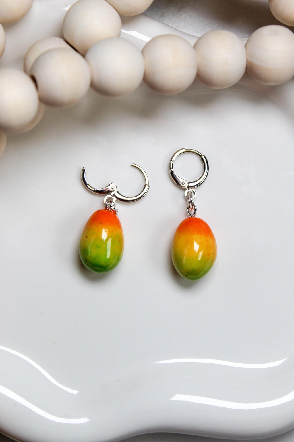 Pair of colorful mango-shaped earrings on a white surface with a blurred background.