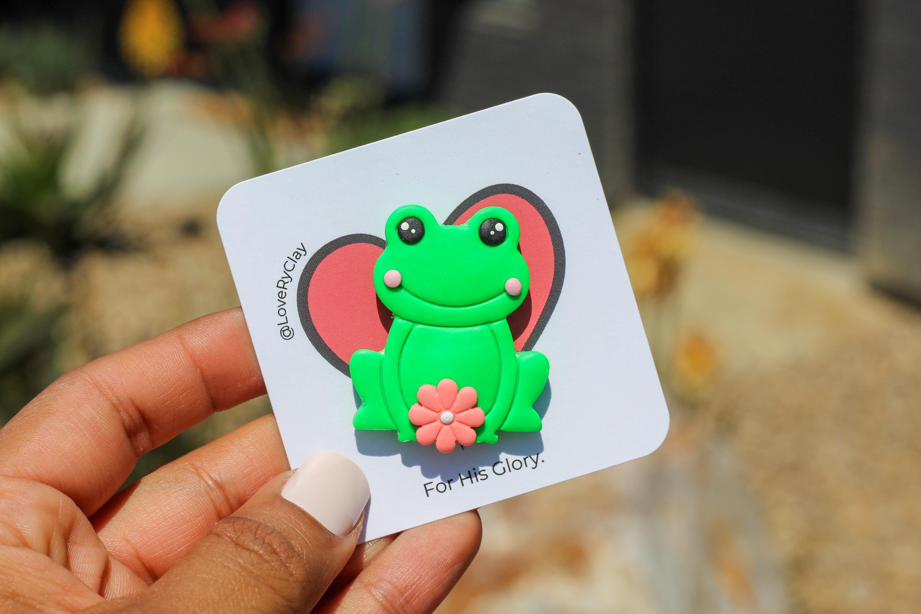 Hand holding a card with a green frog pin blurred background