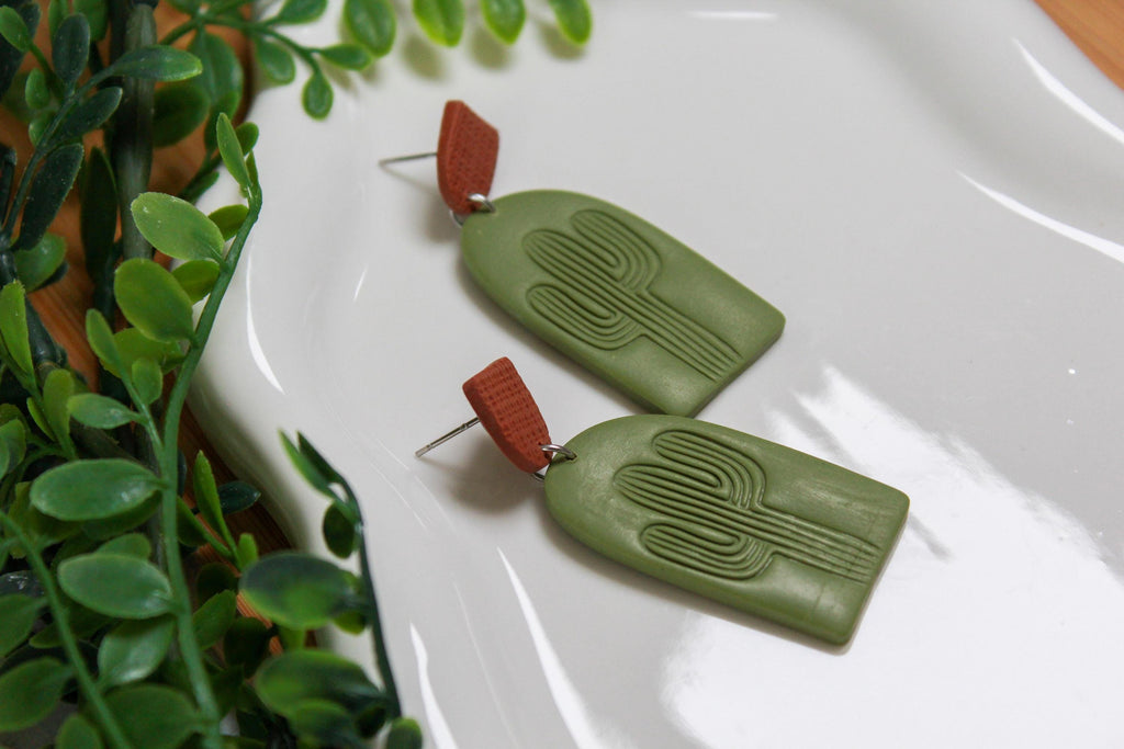 Green earrings with brown accents on a white surface with green leaves in the background