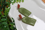 Green earrings with brown accents on a white surface with green leaves in the background