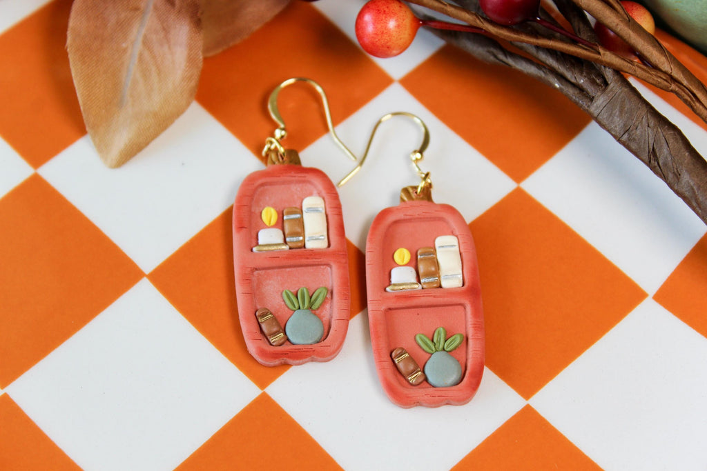 Pair of orange earrings with gold accents on a checkered orange and white surface.