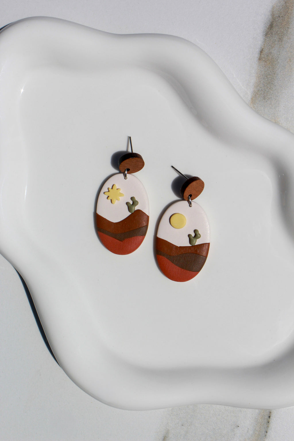 Pair of earrings with desert landscape design on a white ceramic dish