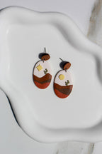 Pair of earrings with desert landscape design on a white ceramic dish