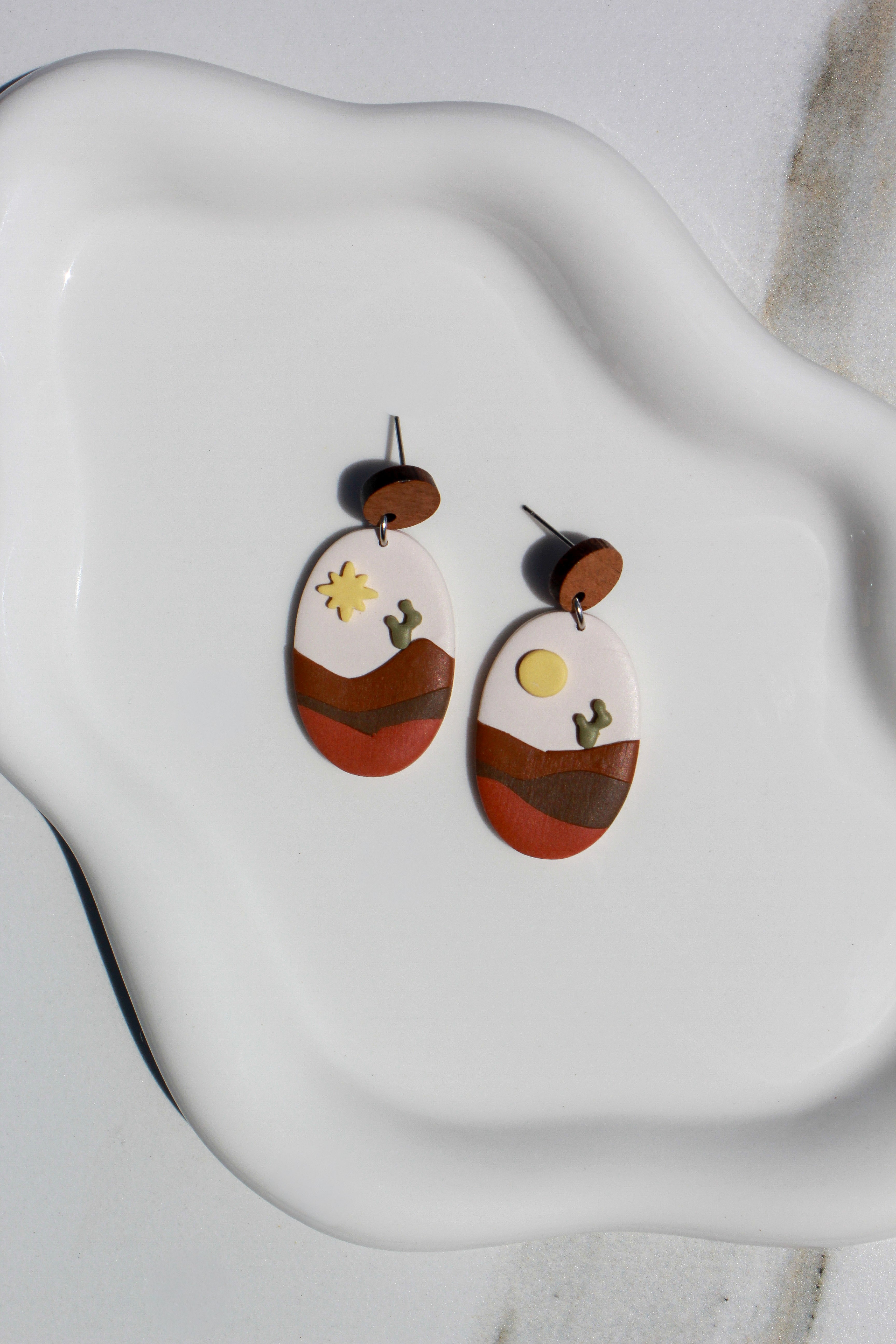 Pair of earrings with desert landscape design on a white ceramic dish