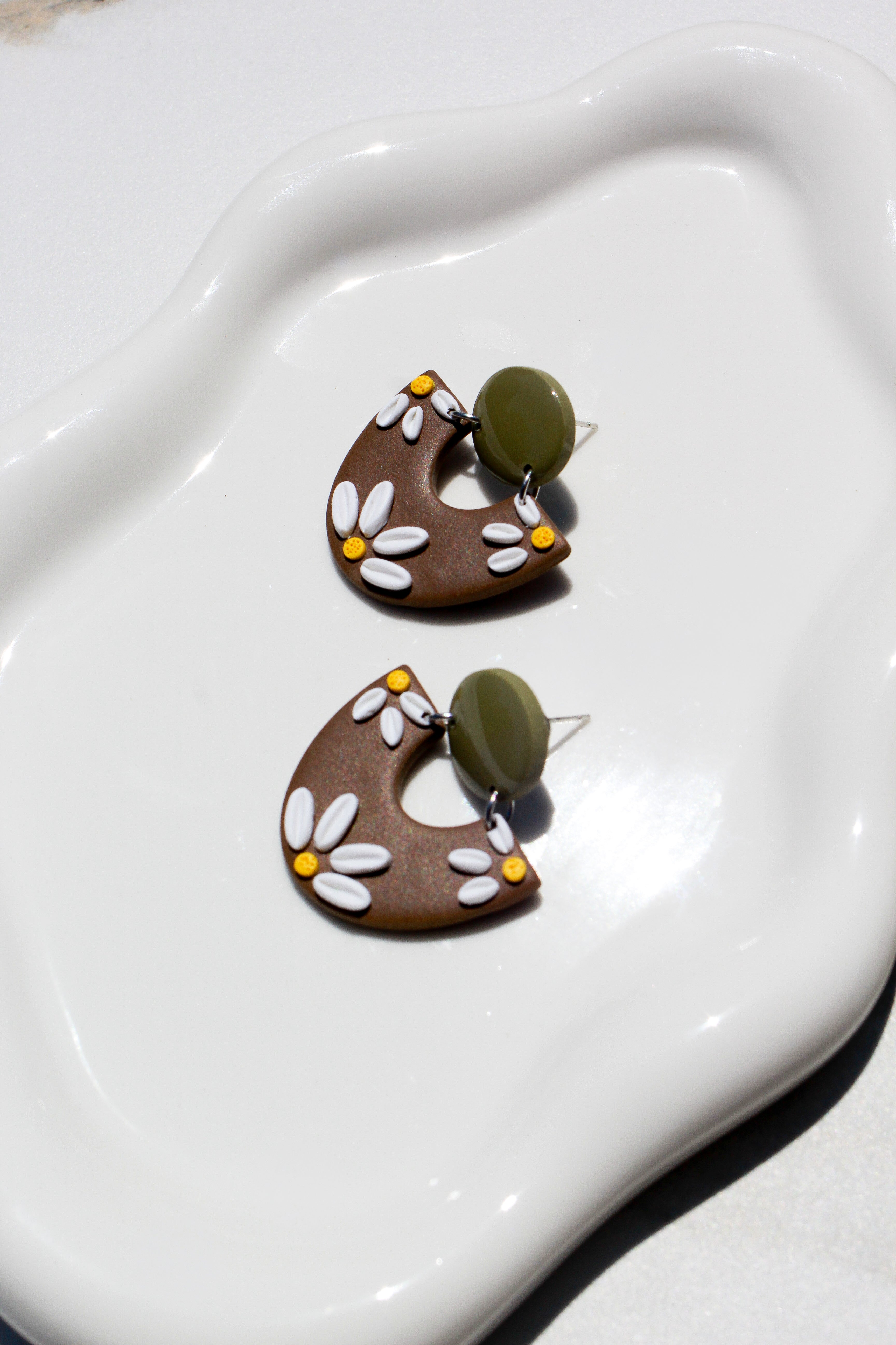 Pair of brown earrings with floral patterns on a white dish
