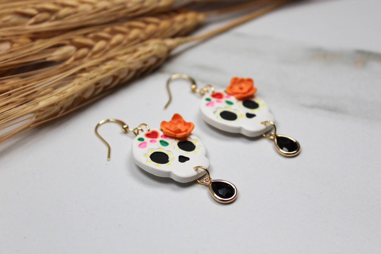 Pair of sugar skull earrings with colorful accents on a light surface.