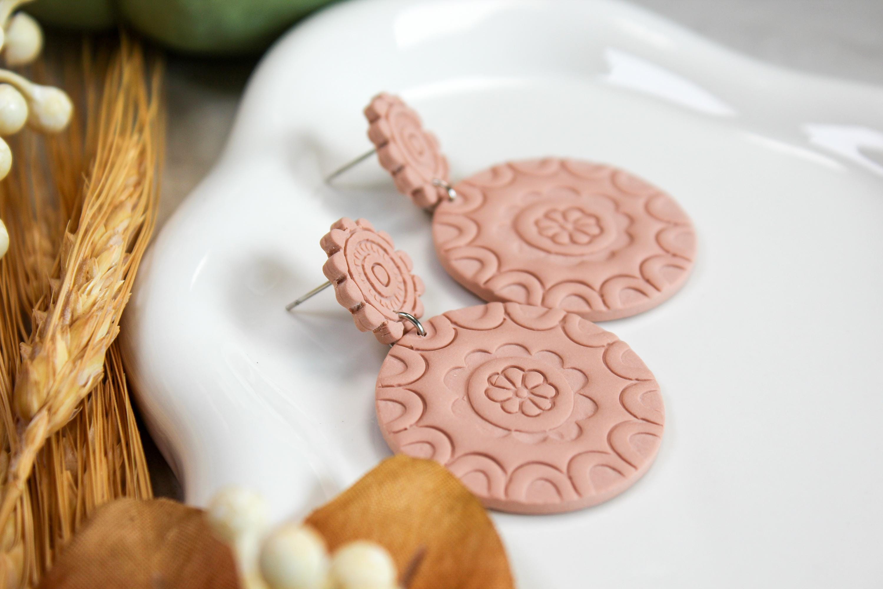 Pink textured earrings on a white surface with natural elements.