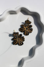 Black and gold floral earrings on a white dish