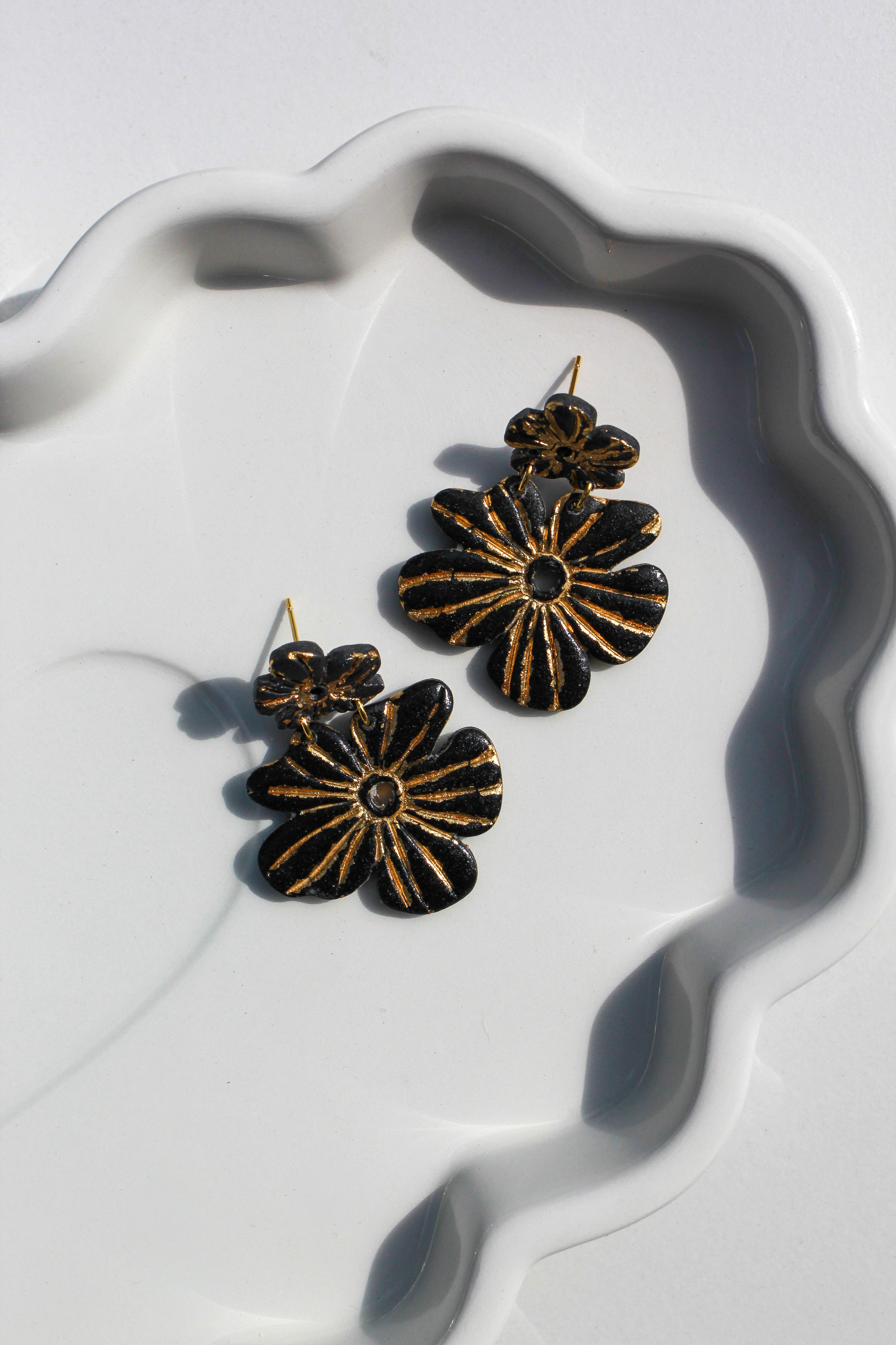 Black and gold floral earrings on a white dish