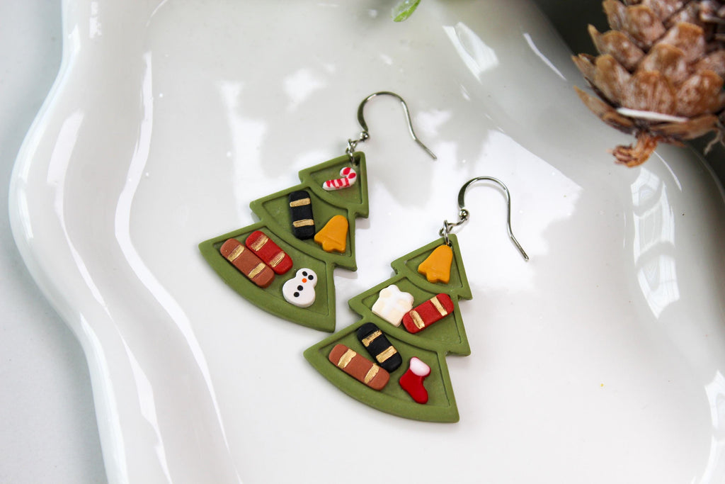 Pair of green Christmas tree-shaped earrings on a white dish