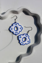 Blue and white floral earrings on a decorative white stand.