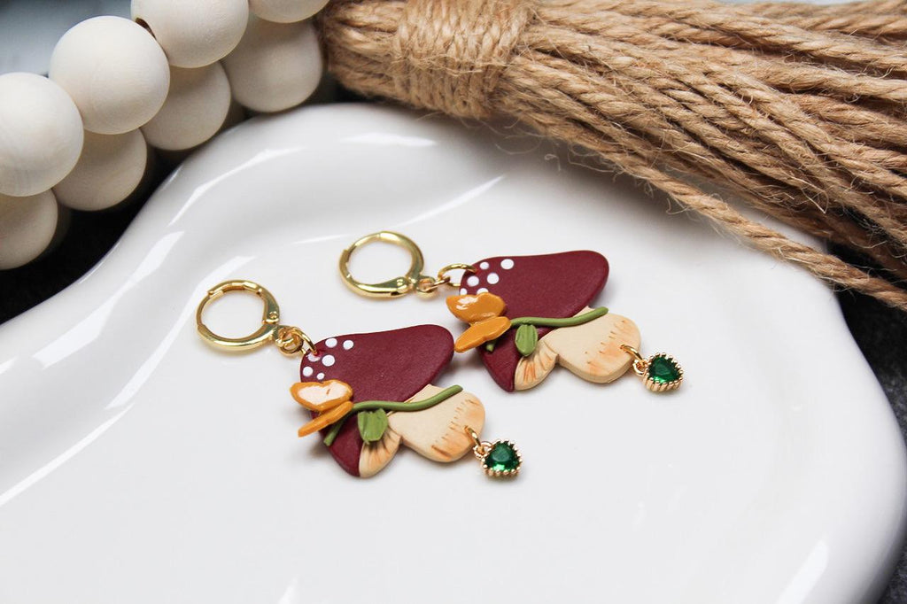 Colorful mushroom earrings on a white dish with decorative elements.