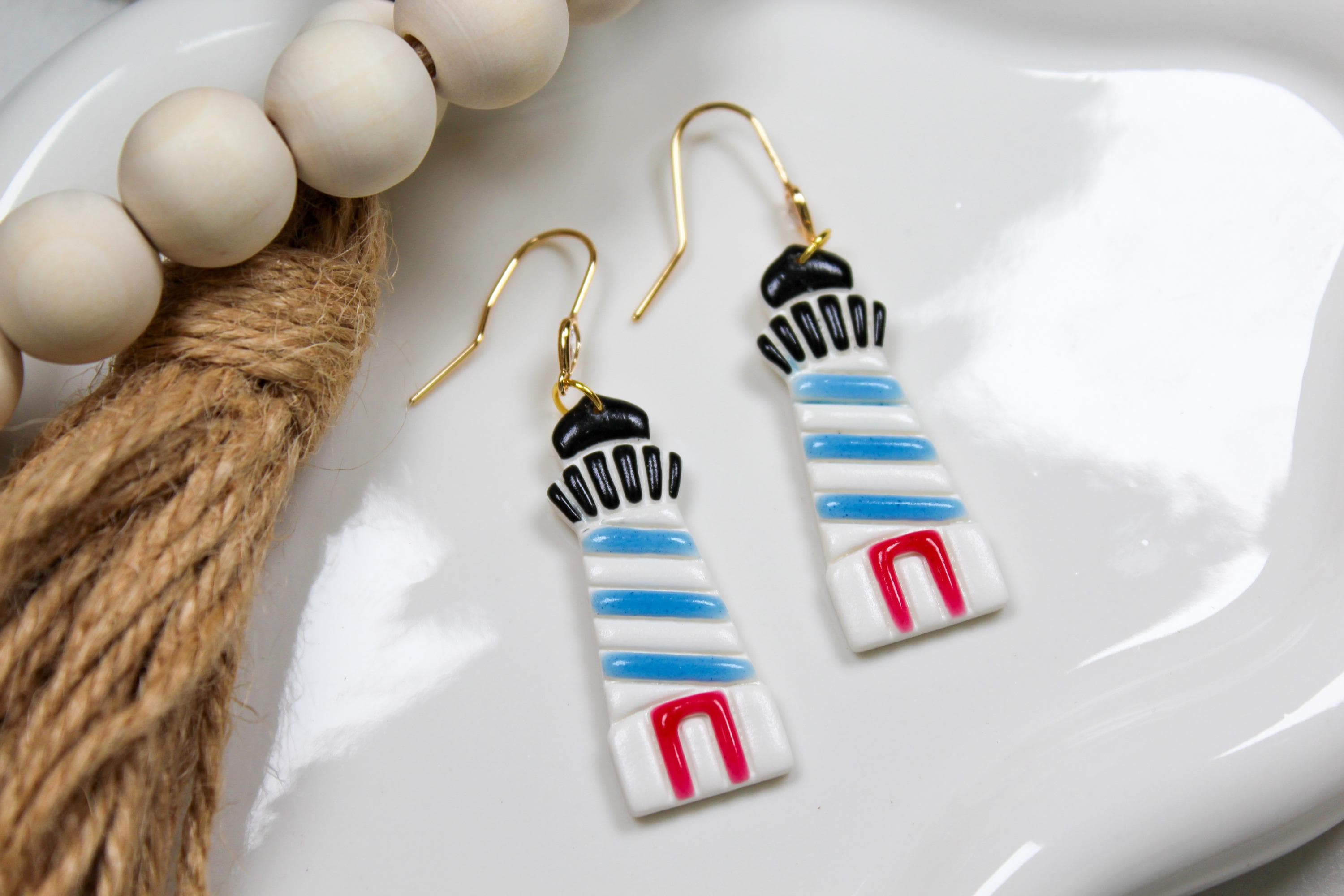 Colorful lighthouse-shaped earrings on a white dish with beads and twine.