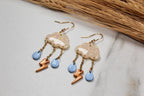 Pair of cloud-shaped earrings with blue accents and gold elements on a light background