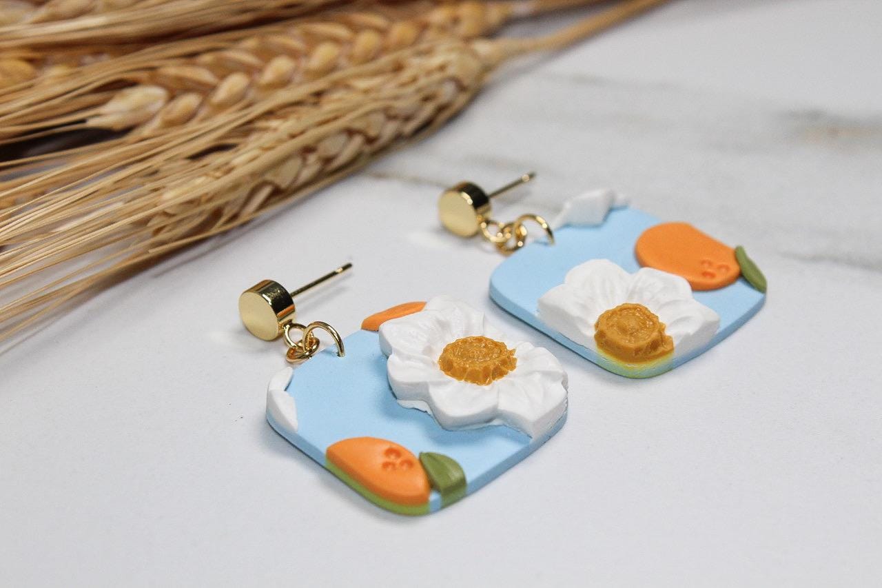 Pair of floral and peaches earrings on a light background with dried grass.