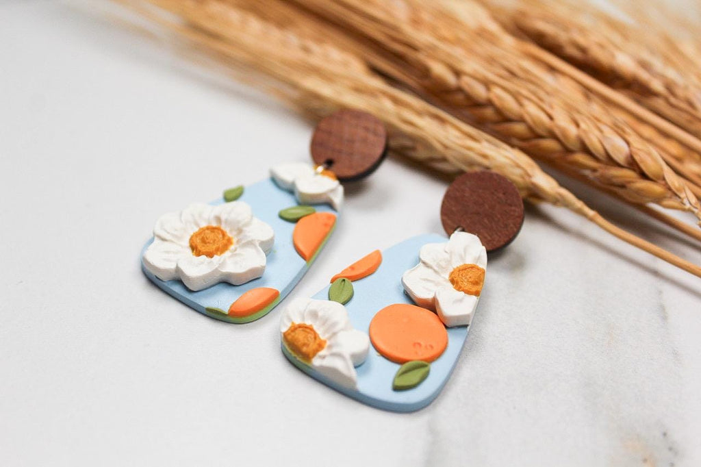 Floral-themed and peach earrings on a light surface with dried wheat stalks.