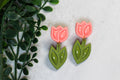 Pink tulip earrings with green leaves on a light background