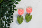 Pink tulip earrings with green leaves on a light background