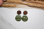 Green earrings with wooden tops on a white surface with wheat stalks.