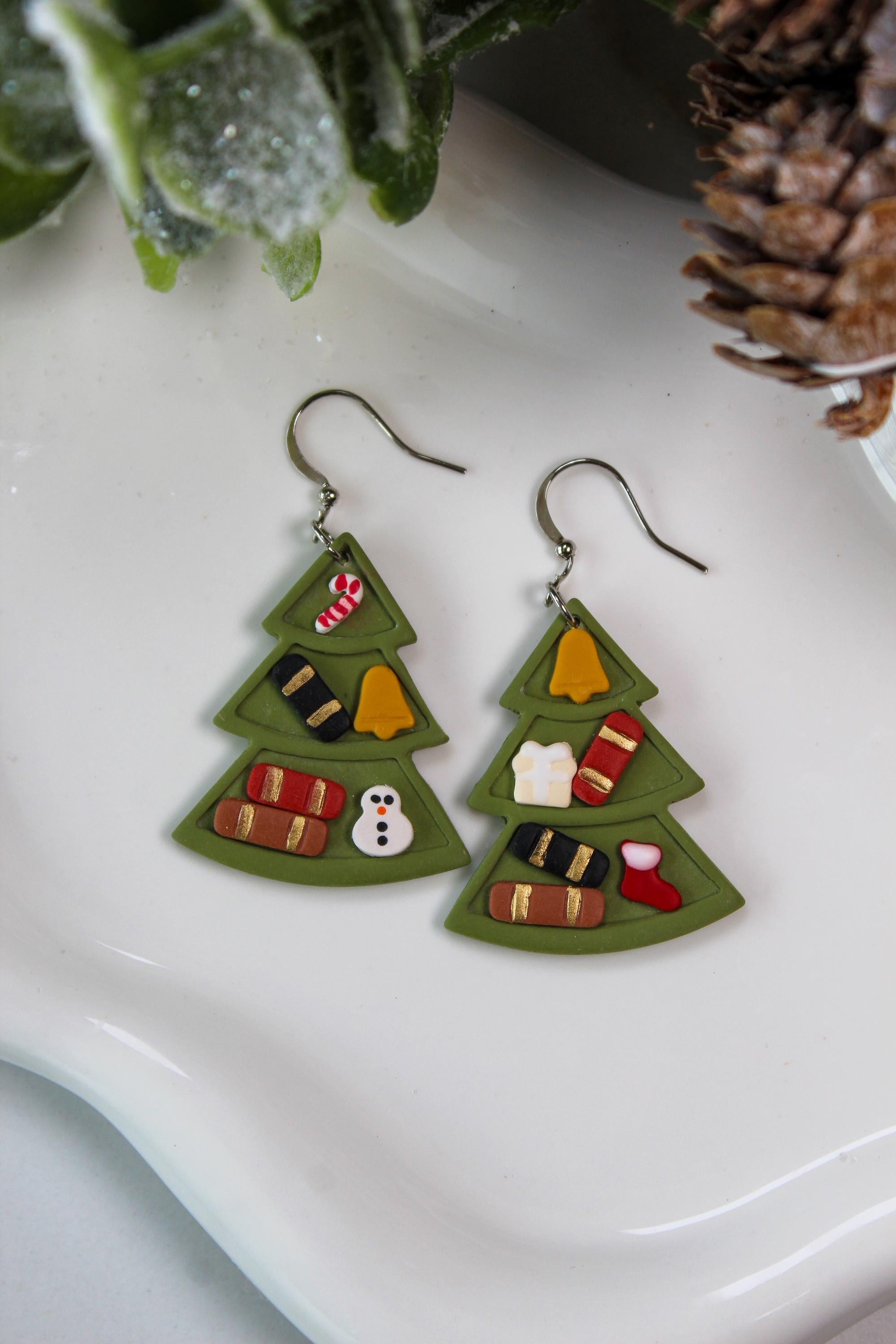 Christmas tree-shaped earrings on a white plate with decorative elements.