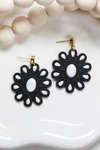 Black flower-shaped earrings with white centers on a white dish.