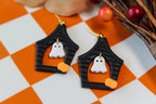Halloween-themed haunted house earrings with ghost designs on a checkered background