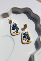 Pair of earrings with blueberry design on a white dish