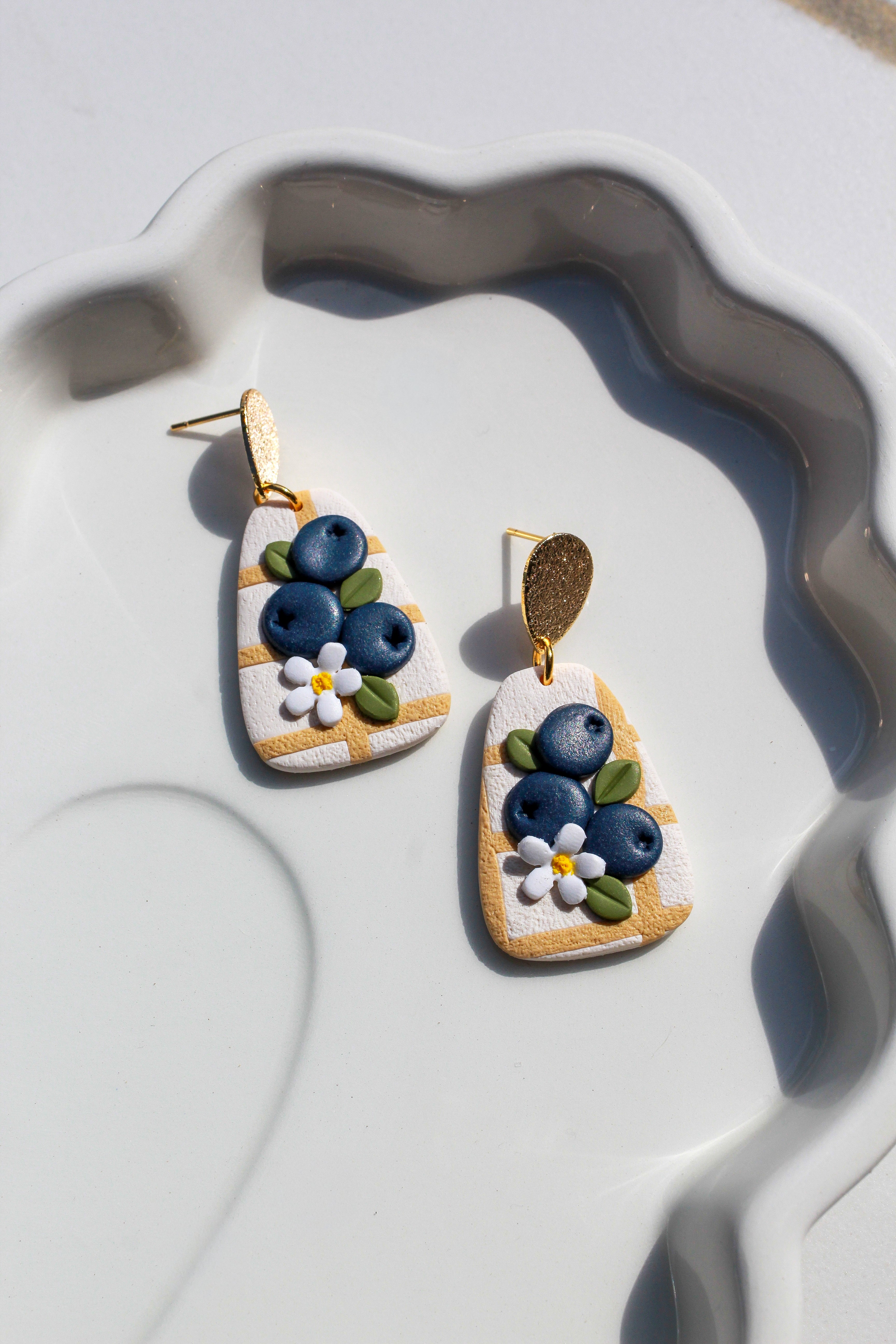 Pair of earrings with blueberry design on a white dish