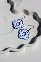 Pair of blue and white floral earrings on a decorative white surface.