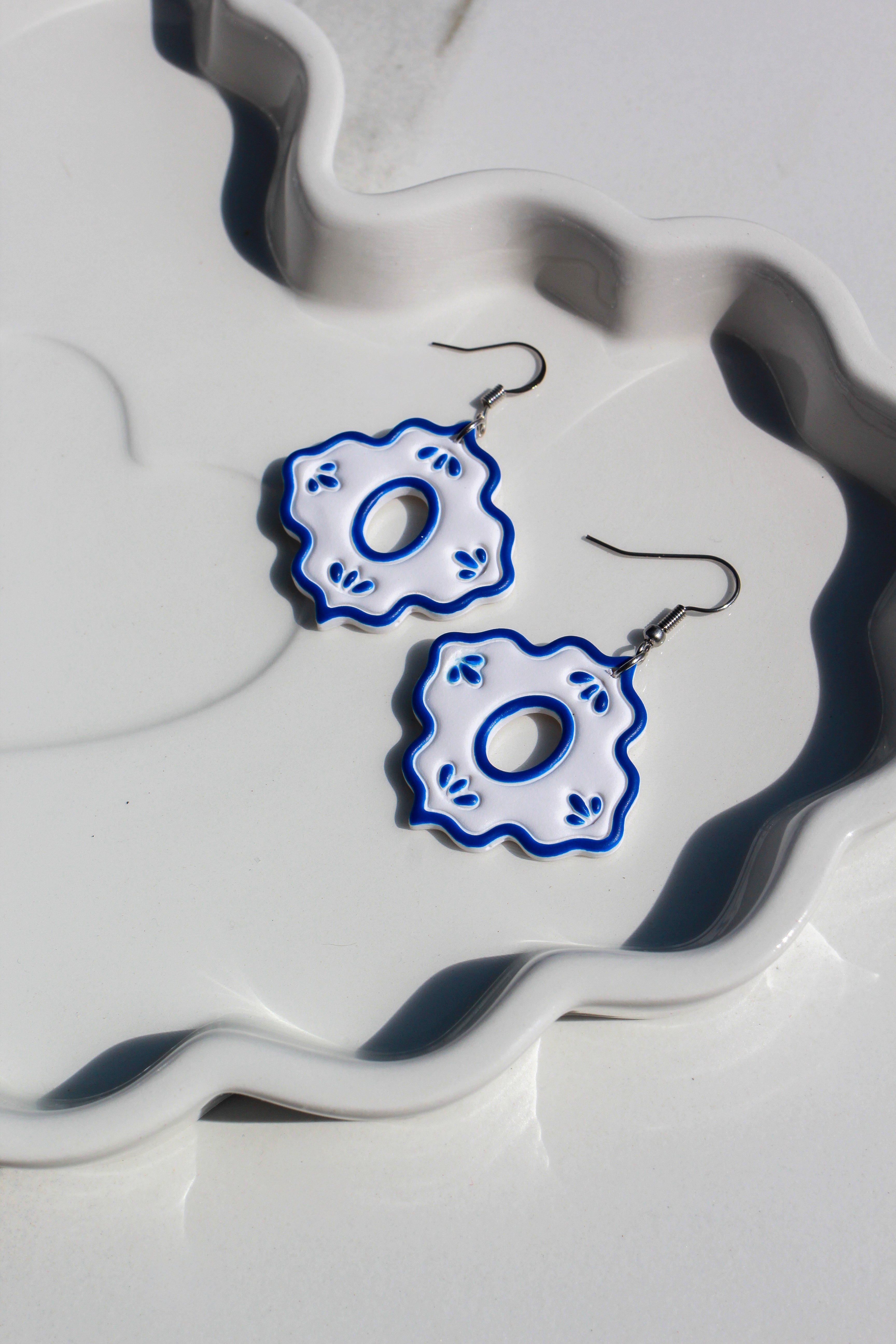 Pair of blue and white floral earrings on a decorative white surface.