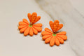 Orange flower-shaped earrings on a light beige background