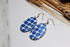 Blue and white patterned earrings on a light surface with dried plants in the background