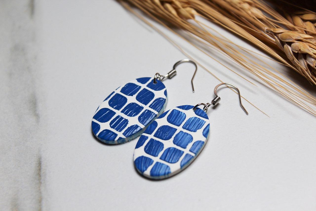 Blue and white patterned earrings on a light surface with dried plants in the background