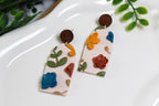 Colorful floral earrings on a white surface with green leaves in the background