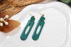 Teal earrings on a white dish with leaves in the background