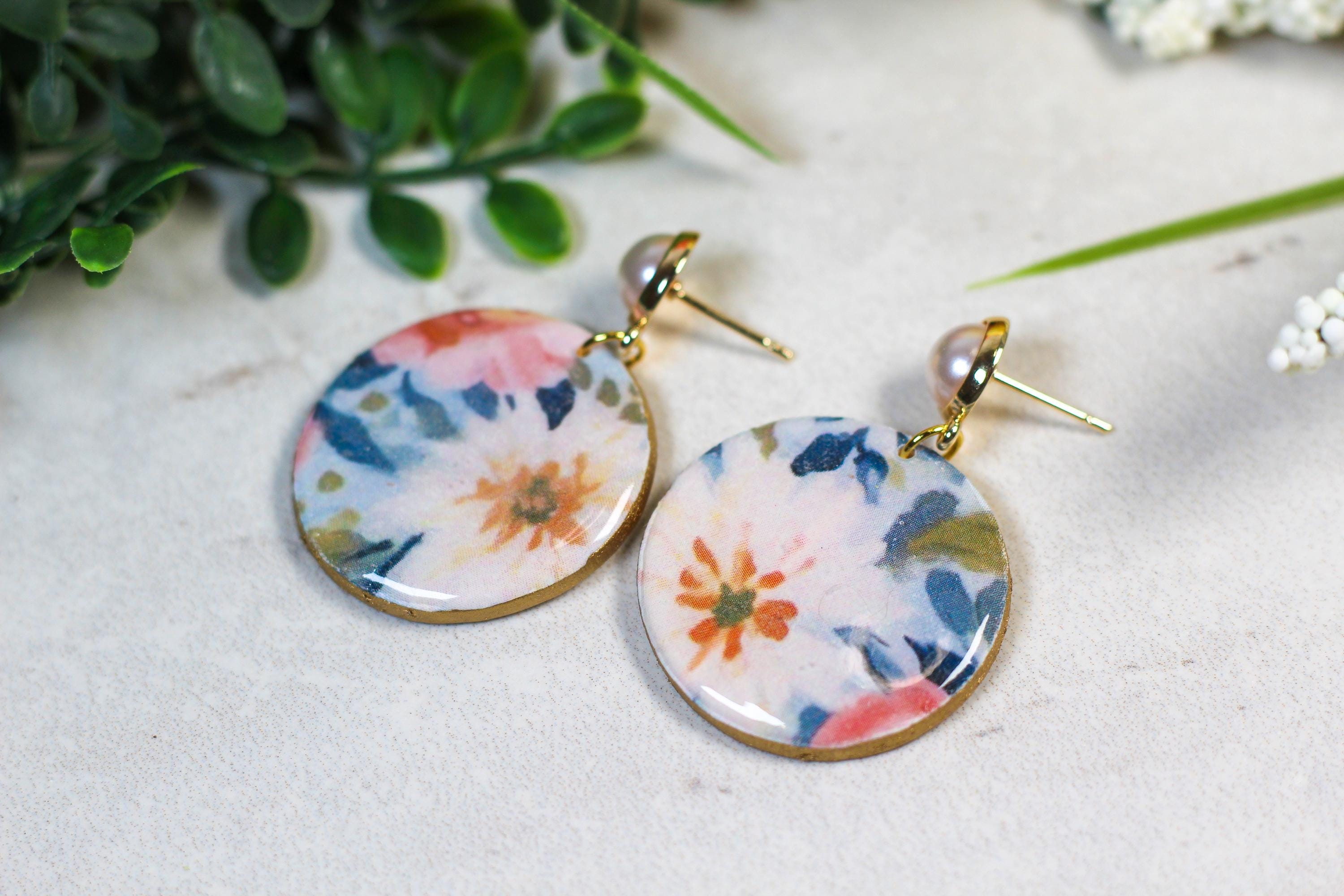 Floral patterned earrings on a light surface with greenery in the background