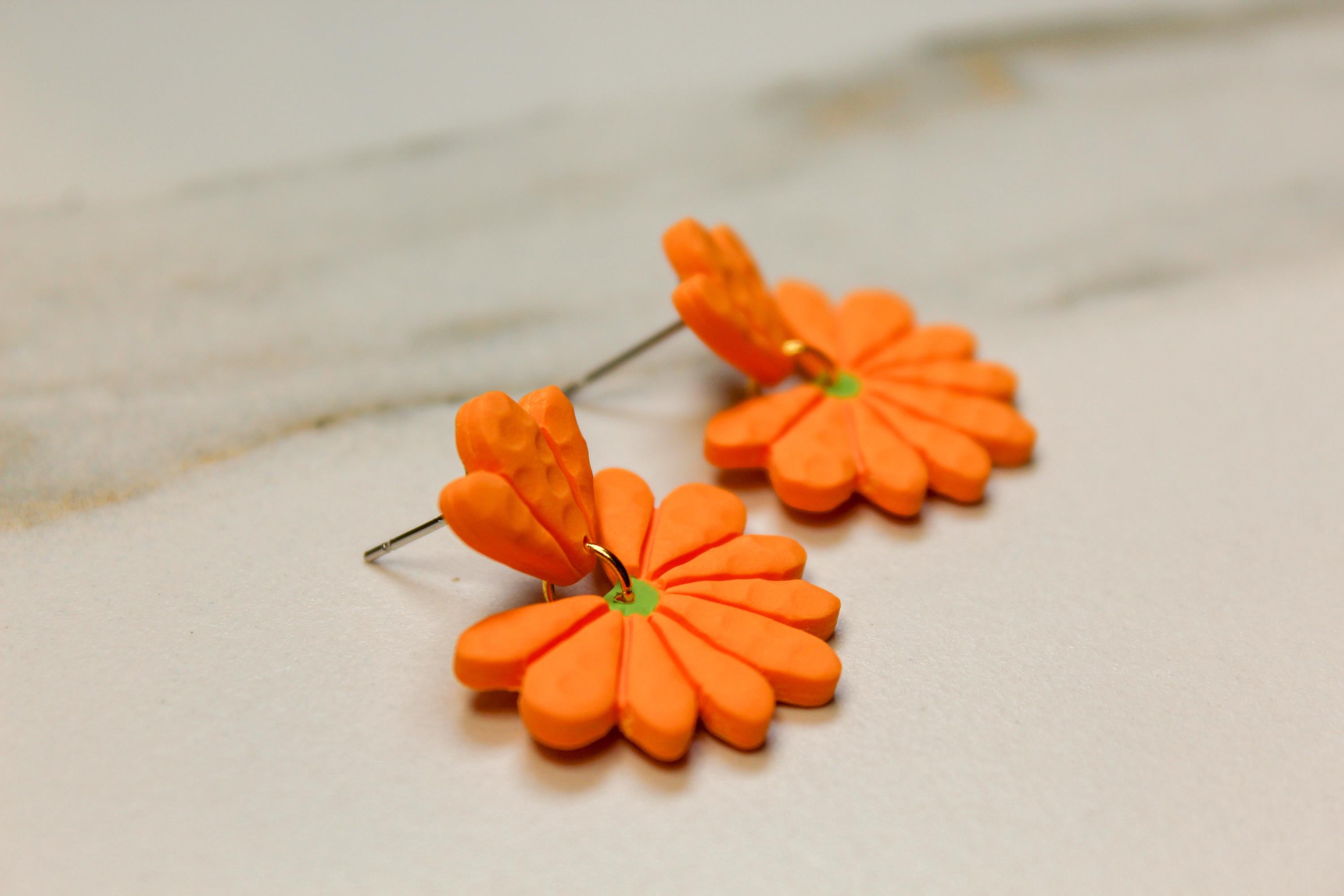 Orange flower-shaped earrings on a light wooden surface