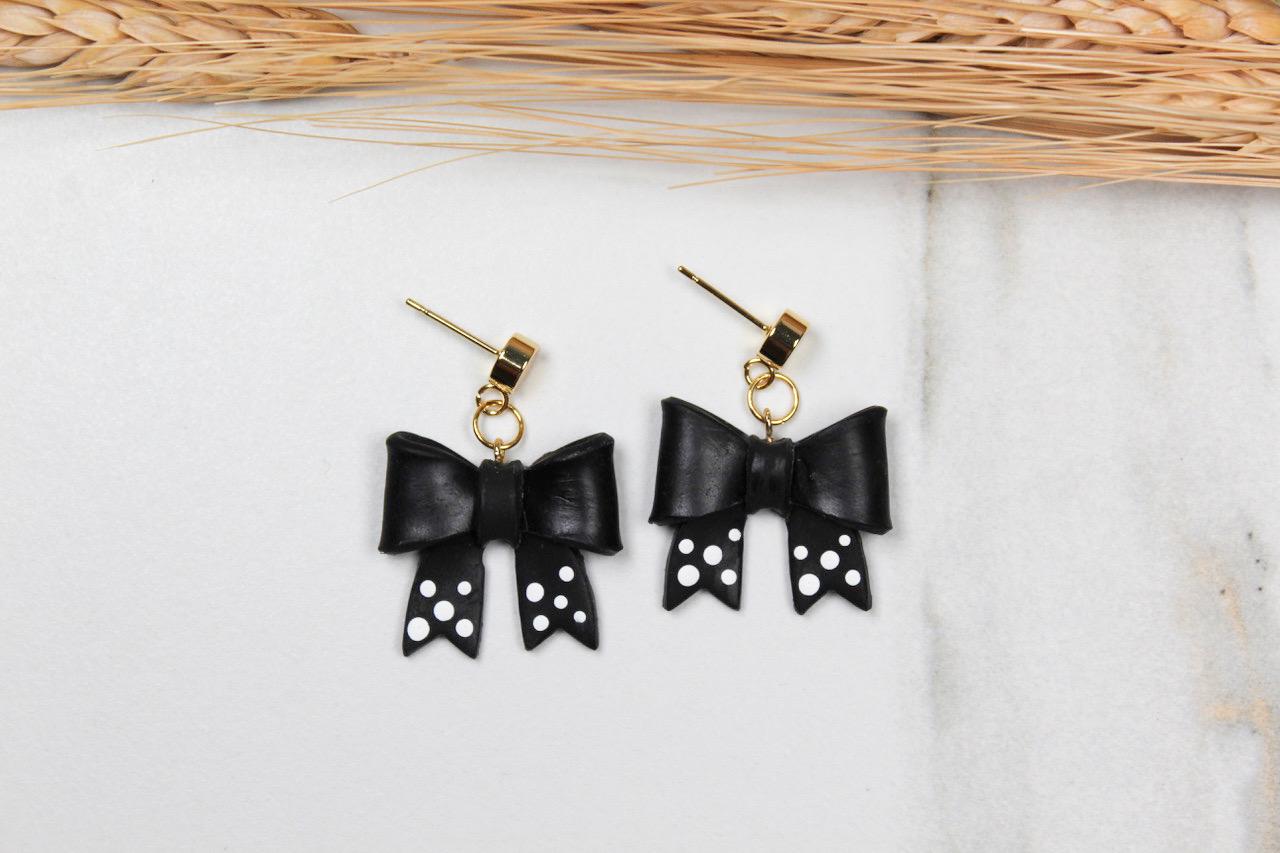 Black bow-shaped earrings with gold accents on a light background
