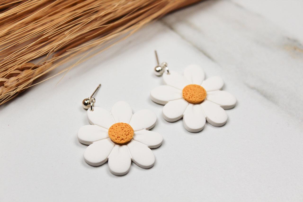 White daisy-shaped earrings with orange centers on a light surface.